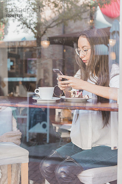 Frau mit Kuchen  die ihr Handy in einem Café überprüft.