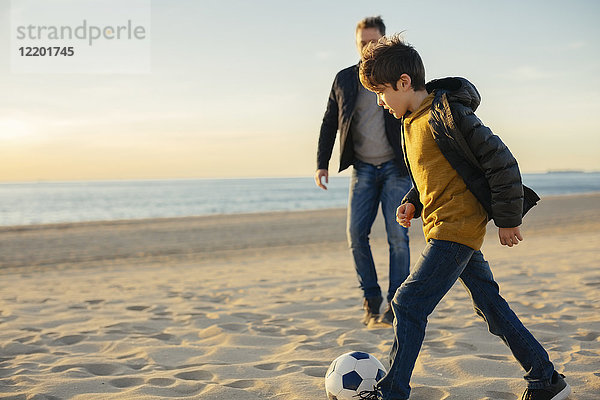 Vater und Sohn spielen Fußball am Strand