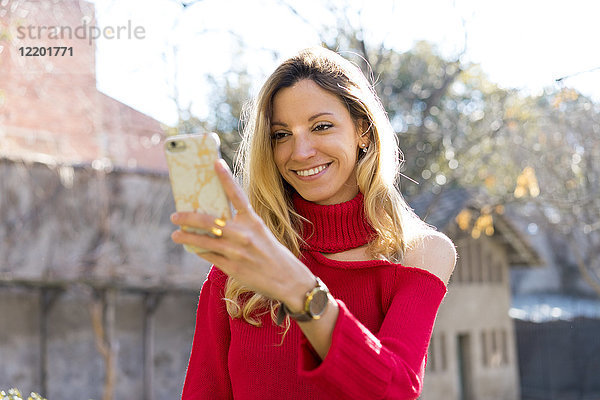 Porträt einer lächelnden jungen Frau mit Blick auf das Smartphone im Freien