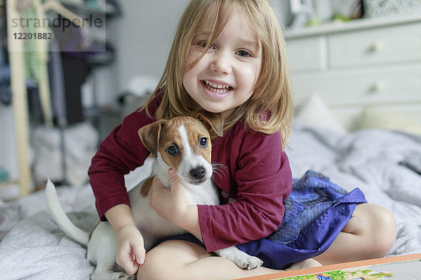 Porträt eines fröhlichen kleinen Mädchens auf dem Bett mit Jack Russel Terrier Welpen