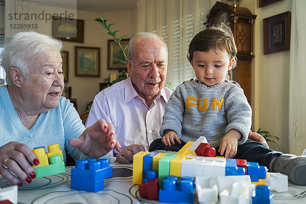 Urgroßeltern und kleines Mädchen beim Spielen mit Plastikbausteinen zu Hause