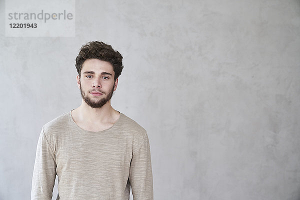 Porträt eines selbstbewussten jungen Mannes vor grauer Wand