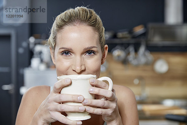 Porträt einer lächelnden blonden Frau in der Küche mit Kaffeetasse