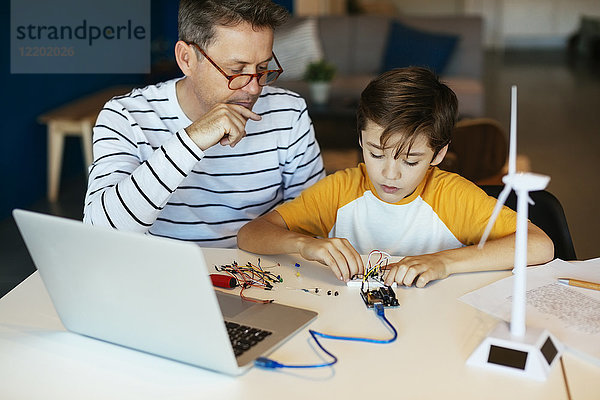 Vater und Sohn bauen einen Baukasten mit Laptop und Windturbinenmodell zusammen