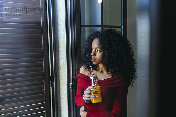 Junge Frau mit Getränk aus dem Fenster schauend