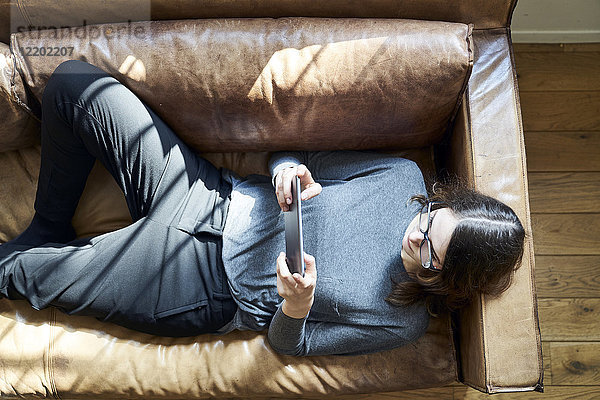Junge Frau auf der Couch liegend mit Tablette