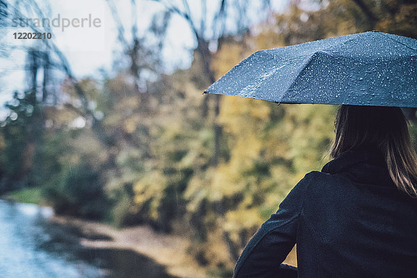 Rückansicht der jungen Frau mit nassem Regenschirm im Herbst