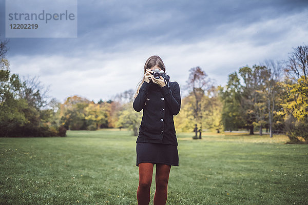 Junge Frau fotografiert mit Kamera auf einer Wiese im Herbstpark