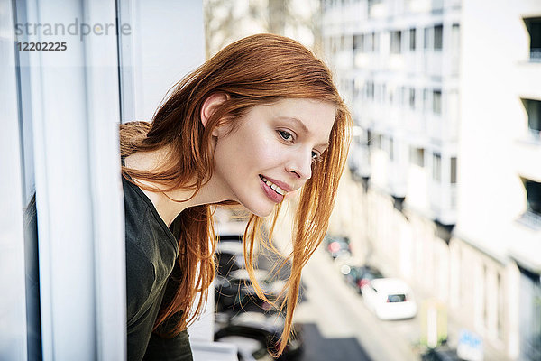 Porträt einer lächelnden rothaarigen Frau  die sich aus dem Fenster lehnt.