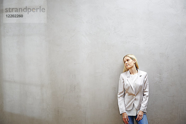 Entspannte Geschäftsfrau vor grauer Wand stehend