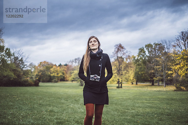 Portrait einer jungen Frau mit Kamera auf einer Wiese im herbstlichen Park