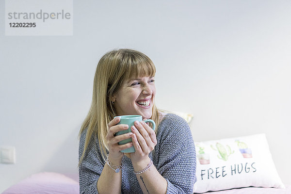 Porträt der lachenden jungen Frau mit Kaffeetasse zu Hause