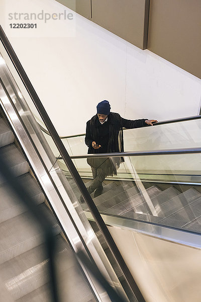 Italien  Mailand  Afroamerikaner mit Smartphone auf Rolltreppe