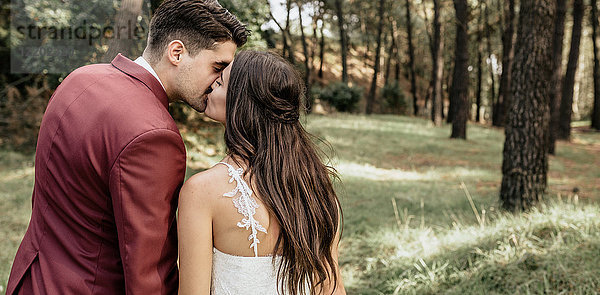 Rückansicht von Braut und Bräutigam beim Küssen im Wald