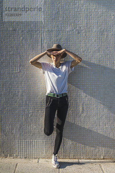 Frau mit Hut vor gekachelter Wand bei Sonneneinstrahlung