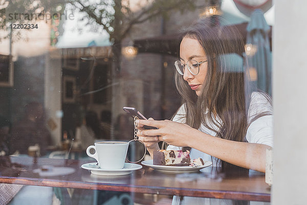 Frau mit Kuchen  die ihr Handy in einem Café überprüft.