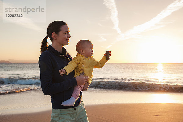 Mutter mit kleiner Tochter am Strand bei Sonnenuntergang