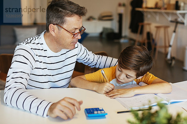 Vater beobachtet Sohn bei den Hausaufgaben am Tisch