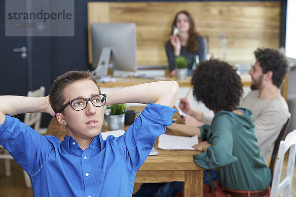 Junger Mann denkt im Büro mit Mitarbeitern im Hintergrund