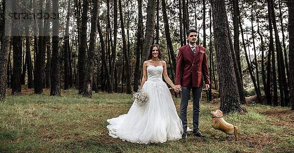 Glückliche Braut und Bräutigam im Wald stehend mit lustigem Hundeballon
