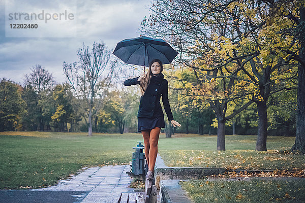 Junge Frau mit Regenschirm auf der Rückenlehne der Bank im Herbstpark