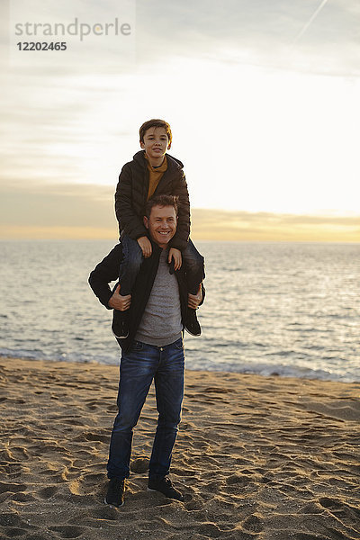 Porträt des Vaters  der seinen Sohn huckepack am Strand trägt.