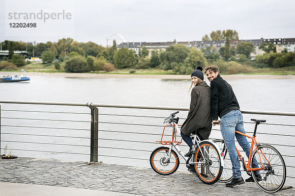 Lächelndes Paar mit Fahrrädern am Flussufer