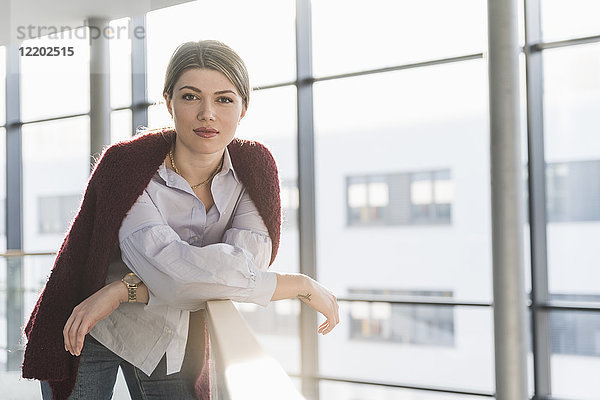 Porträt einer selbstbewussten jungen Frau am Geländer im hellen Bürogebäude