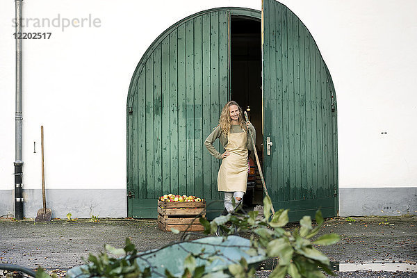 Lächelnde Frau auf einem Bauernhof stehend an einer Kiste mit Äpfeln