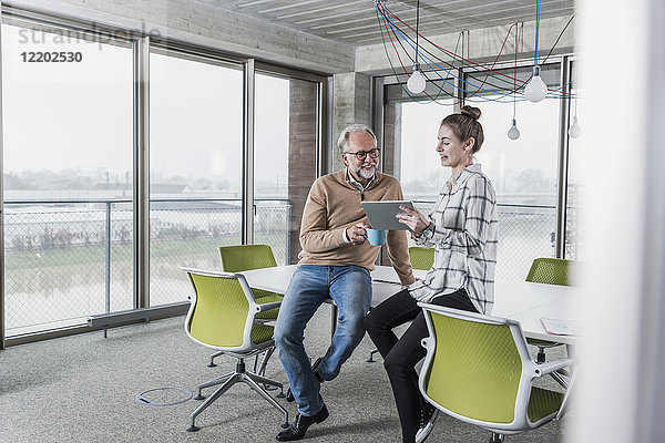 Lässiger reifer Geschäftsmann und junge Frau mit Tablette im Konferenzraum im Büro