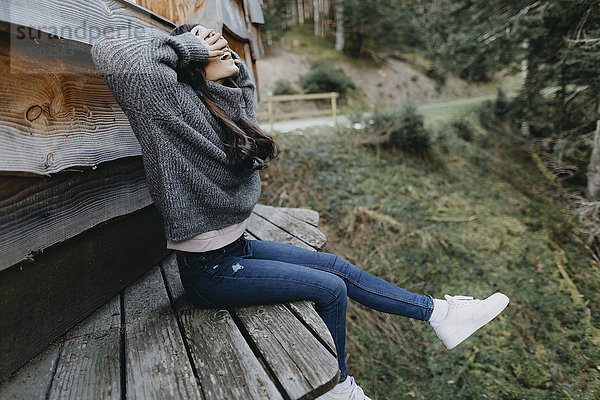 Fröhliche junge Frau in einem Holzhaus in der Natur sitzend