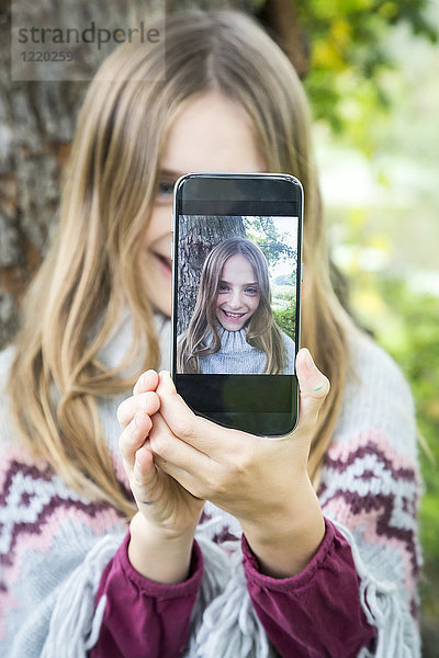 Porträt eines lachenden Mädchens  das sich selbst mit dem Handy fotografiert.