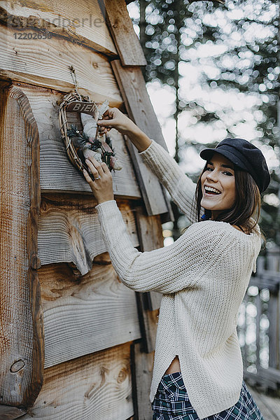 Fröhliche junge Frau schmückt Holzhaus mit Weihnachtsdekoration