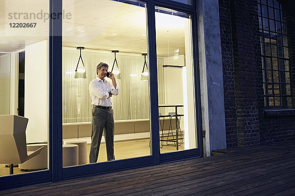 Außenansicht des Menschen mit Smartphone im modernen Gebäude bei Nacht
