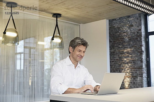 Lächelnder Geschäftsmann mit Laptop im modernen Büro