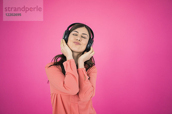 Frau vor der rosa Wand hört Musik über Kopfhörer