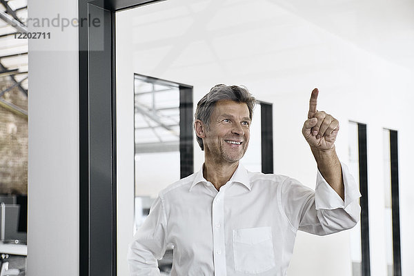 Lächelnder reifer Geschäftsmann berührt Glasscheibe im modernen Büro