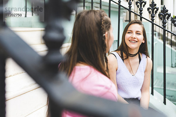 Zwei glückliche Teenager  die auf einer Treppe in der Stadt sitzen und reden.