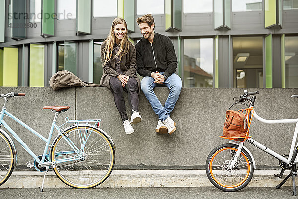 Glückliches Paar mit Fahrrädern an der Wand sitzend