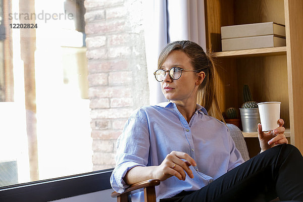 Junge Frau mit Kaffeetasse mit Blick aus dem Bürofenster