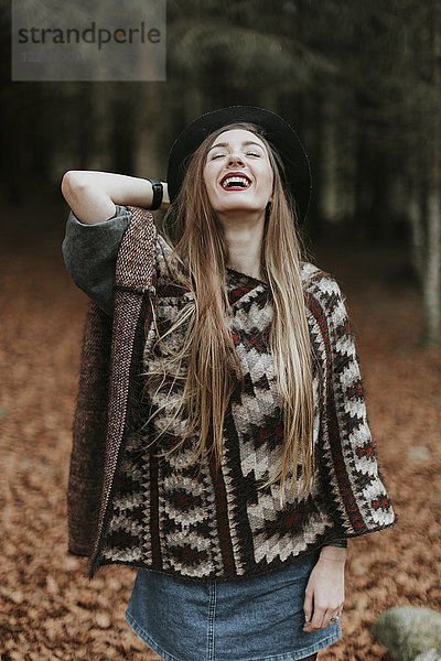 Porträt der lachenden jungen Frau mit Hut und Poncho im Herbstwald