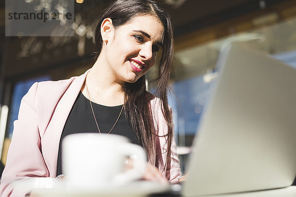 Lächelnde junge Geschäftsfrau mit Laptop in einem Outdoor-Café