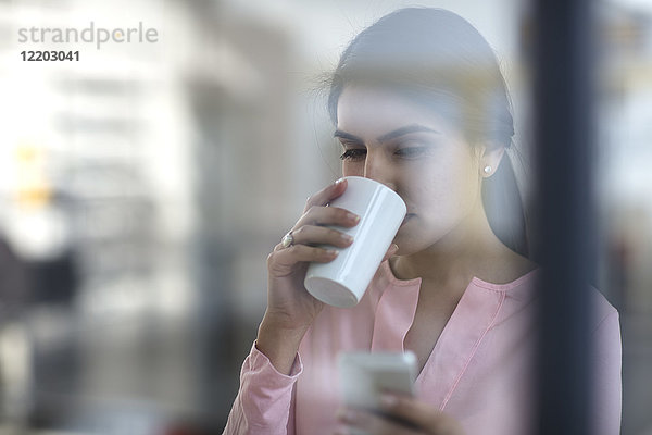 Porträt einer jungen Frau mit Handy und Kaffee im Büro