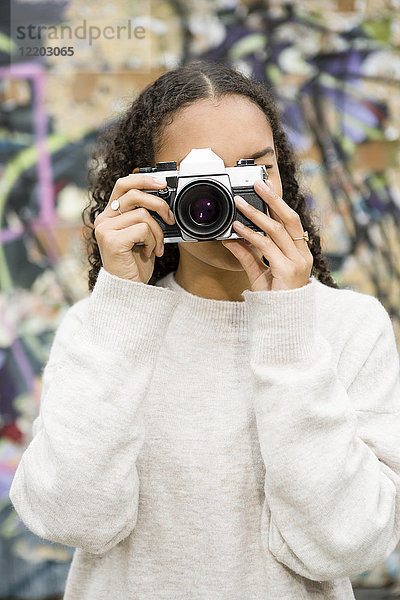 Deutschland  Berlin  junge Frau beim Fotografieren mit einer alten Kamera vor Graffiti