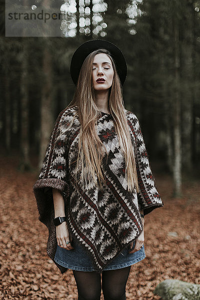 Porträt einer jungen Frau mit Hut und Poncho im herbstlichen Wald