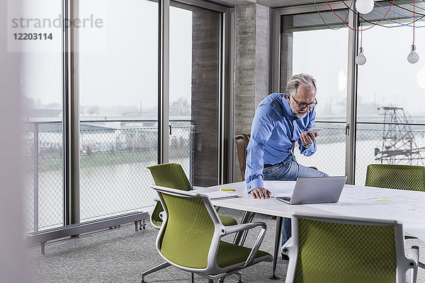 Reife Geschäftsleute mit Laptop und Smartphone im Konferenzraum im Büro