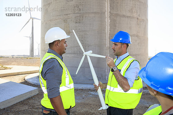Drei Ingenieure mit Windkraftanlagenmodell diskutieren über einen Windpark
