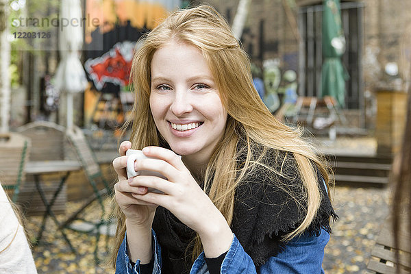Deutschland  Berlin  Porträt einer glücklichen jungen Frau beim Kaffeetrinken im Straßencafé