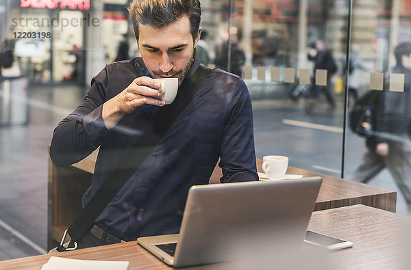 Junger Geschäftsmann in einem Café am Bahnhof mit Kaffee und Laptop