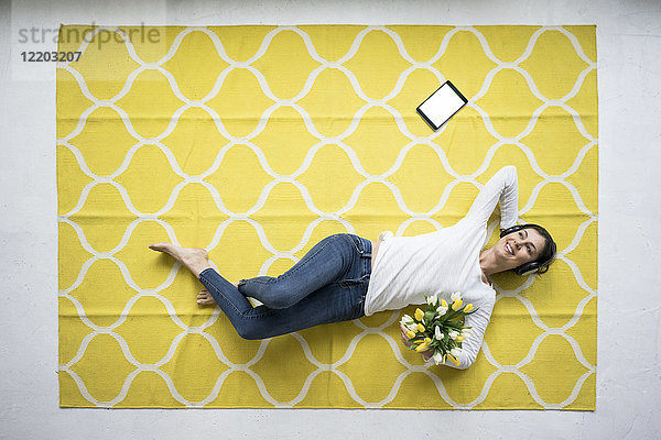 Lächelnde Frau mit Kopfhörer auf Teppich mit Tulpenbüscheln